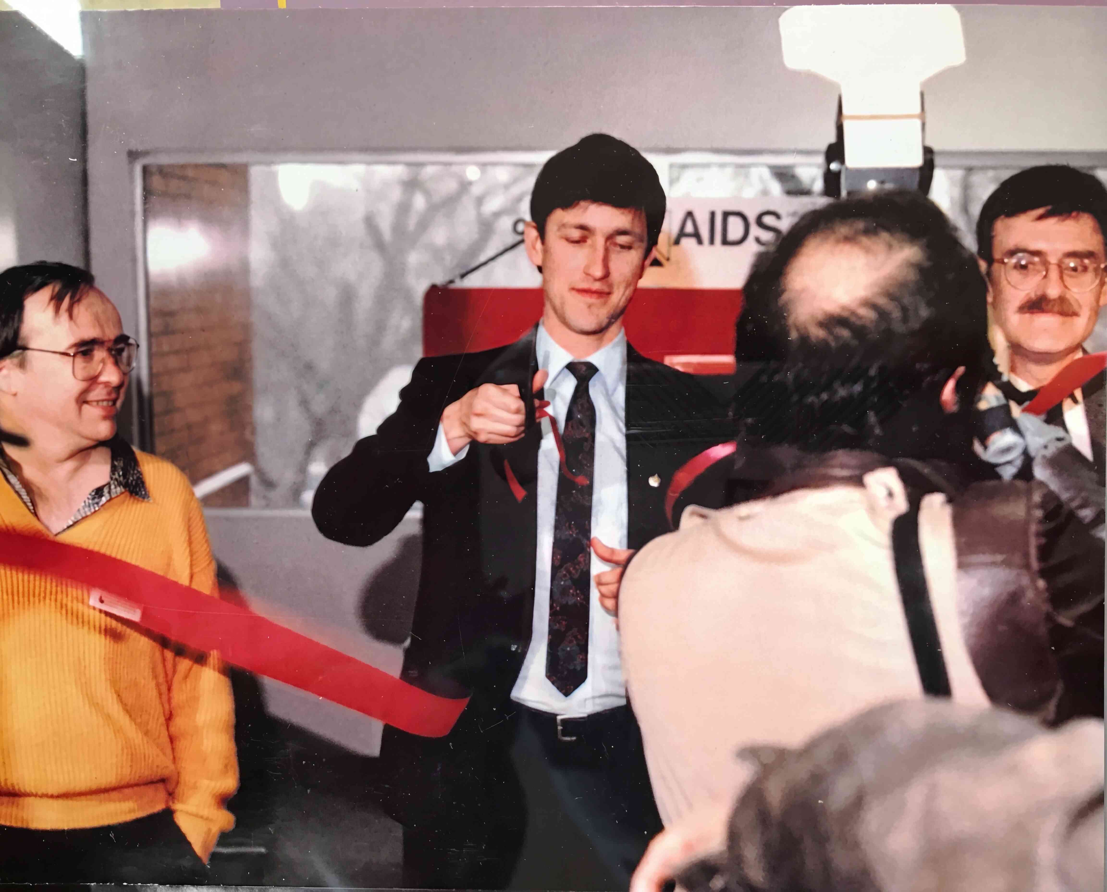 People at a ribbon-cutting ceremony in front of an AIDS-awareness sign