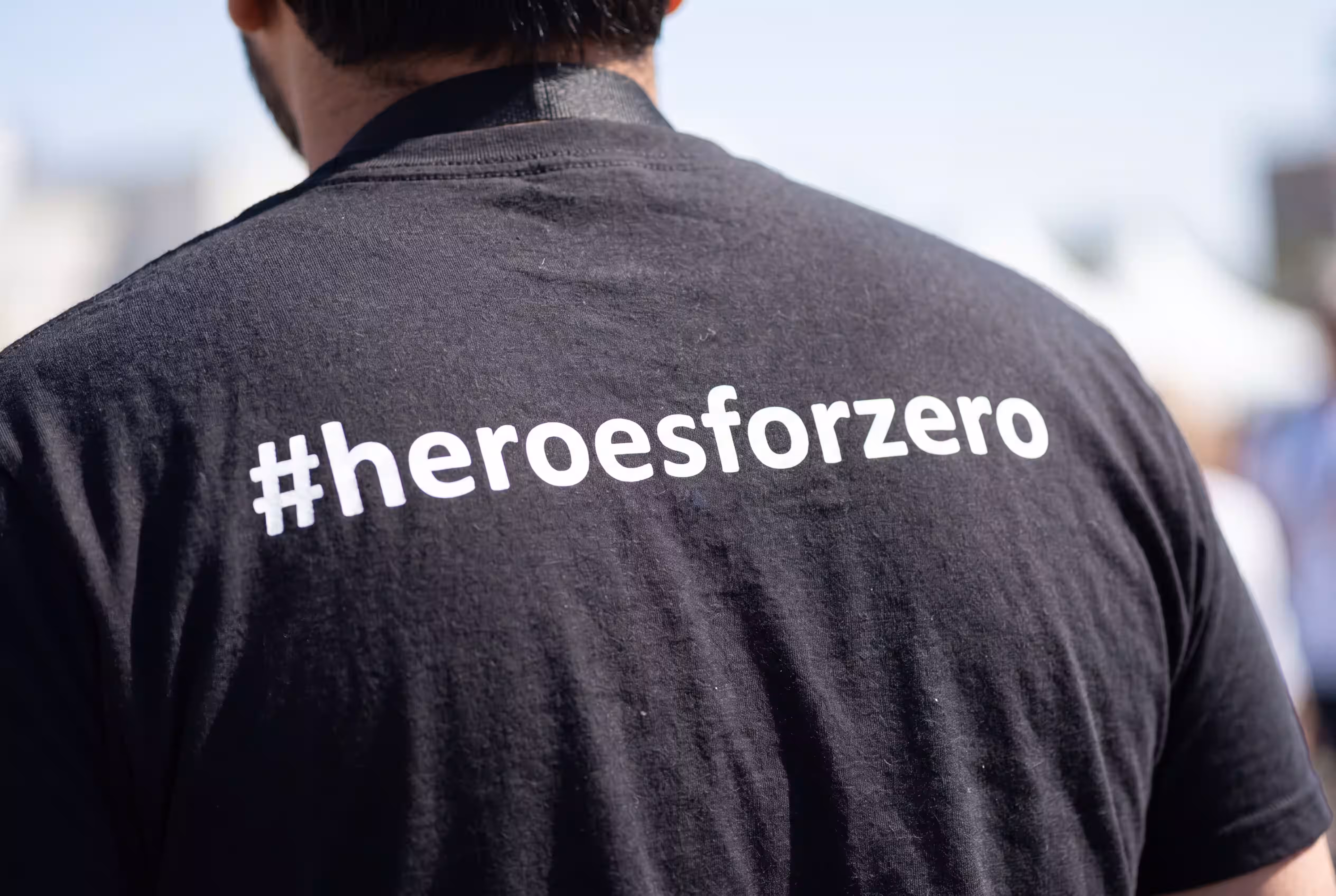 Close-up of a person's back wearing a black #heroesforzero T-shirt at an outdoor event