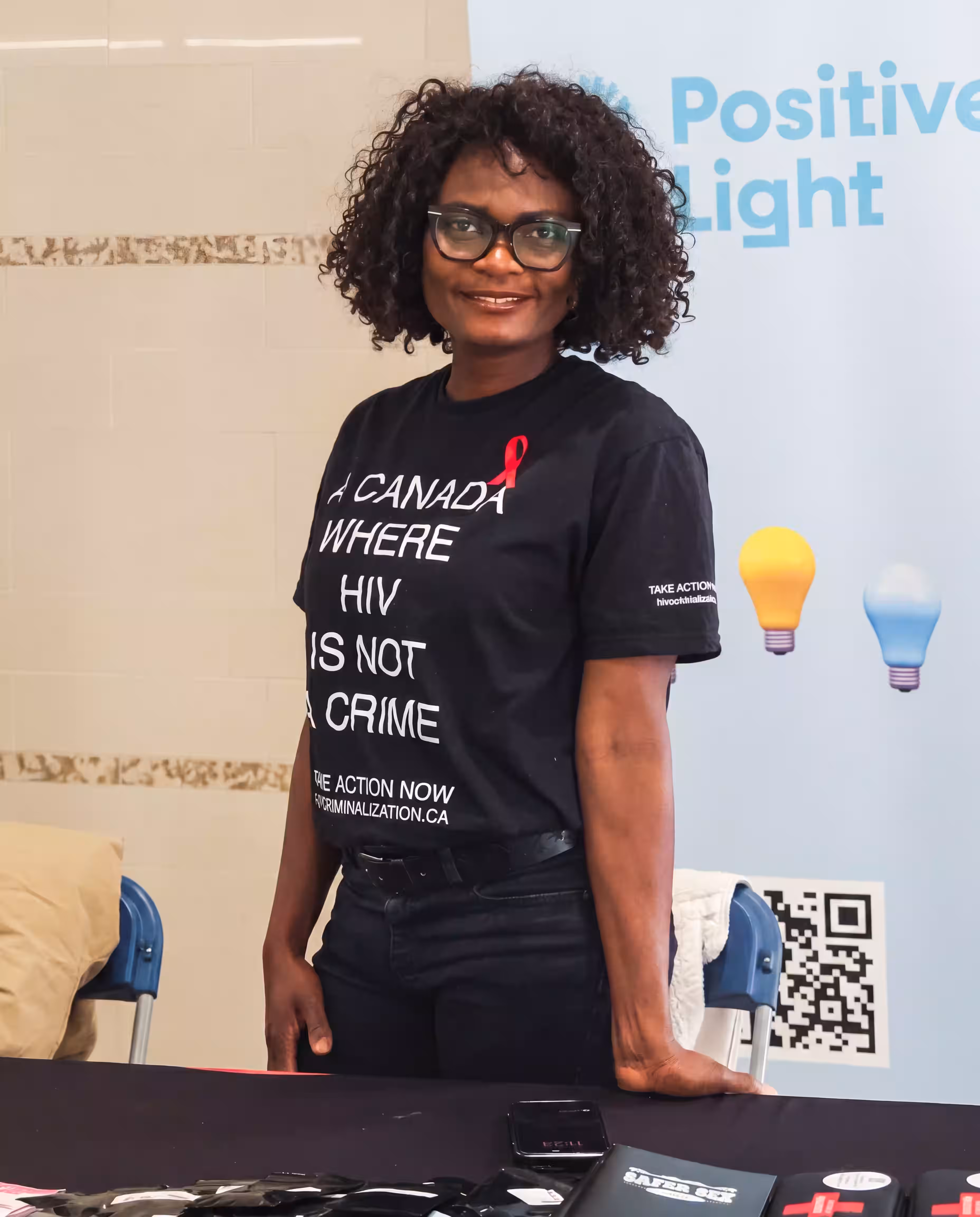 A volunteer at the Positive Light booth wearing an 'A Canada where HIV is not a crime' T-shirt