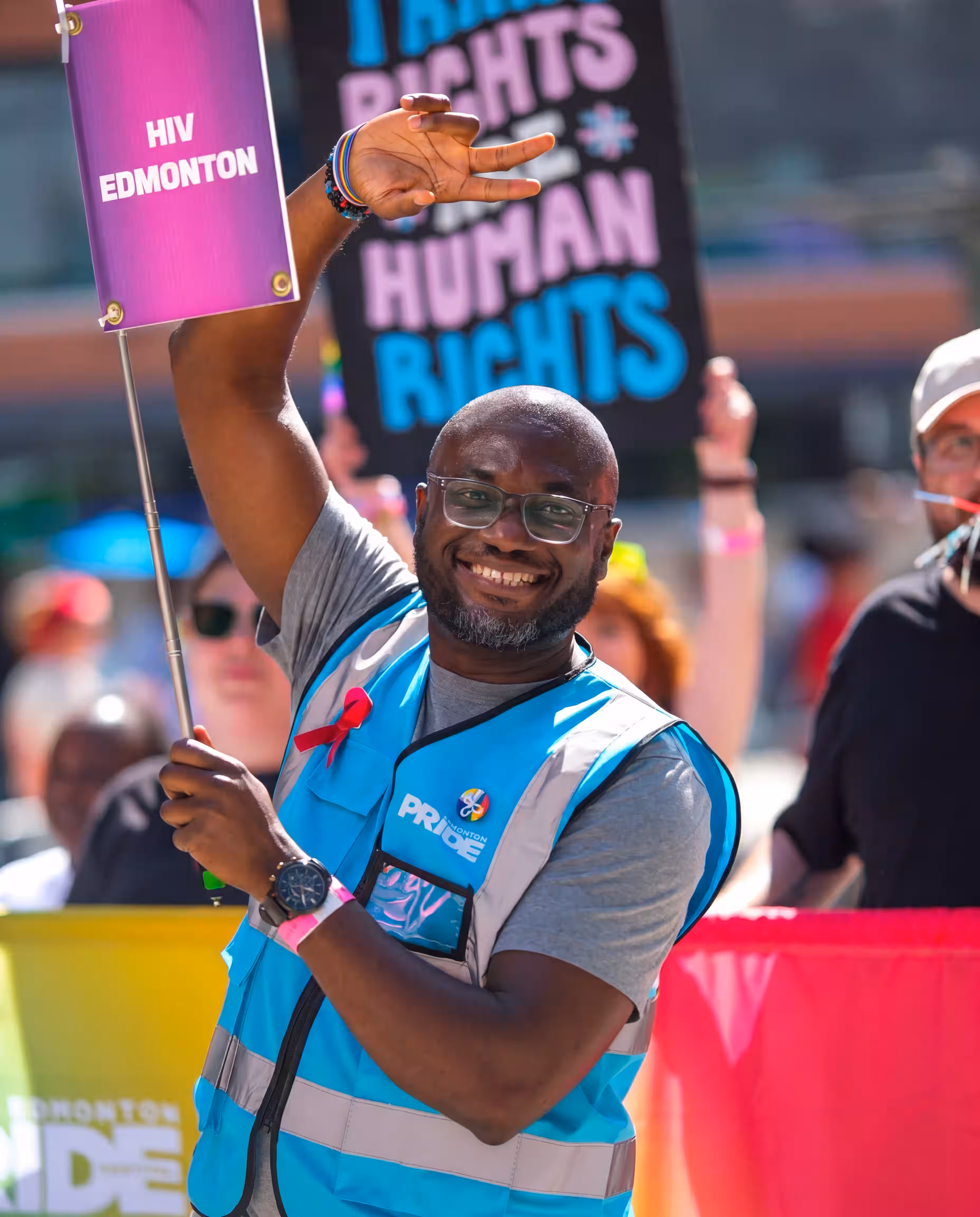 An HIV Edmonton volunteer in a hi-vis vest holding a sign at a Pride parade