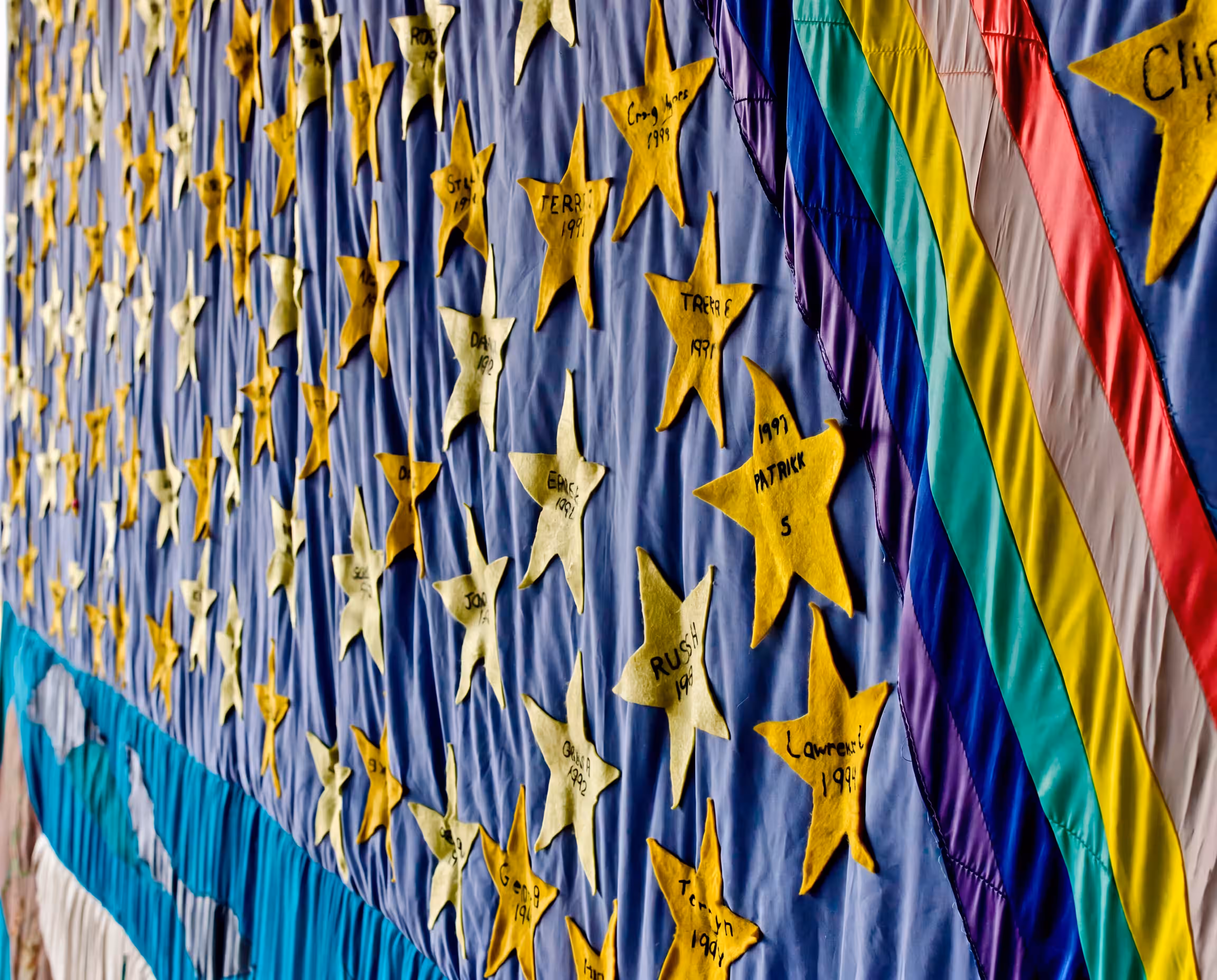 A section of the AIDS Memorial Quilt with gold commemorative stars and rainbow ribbons