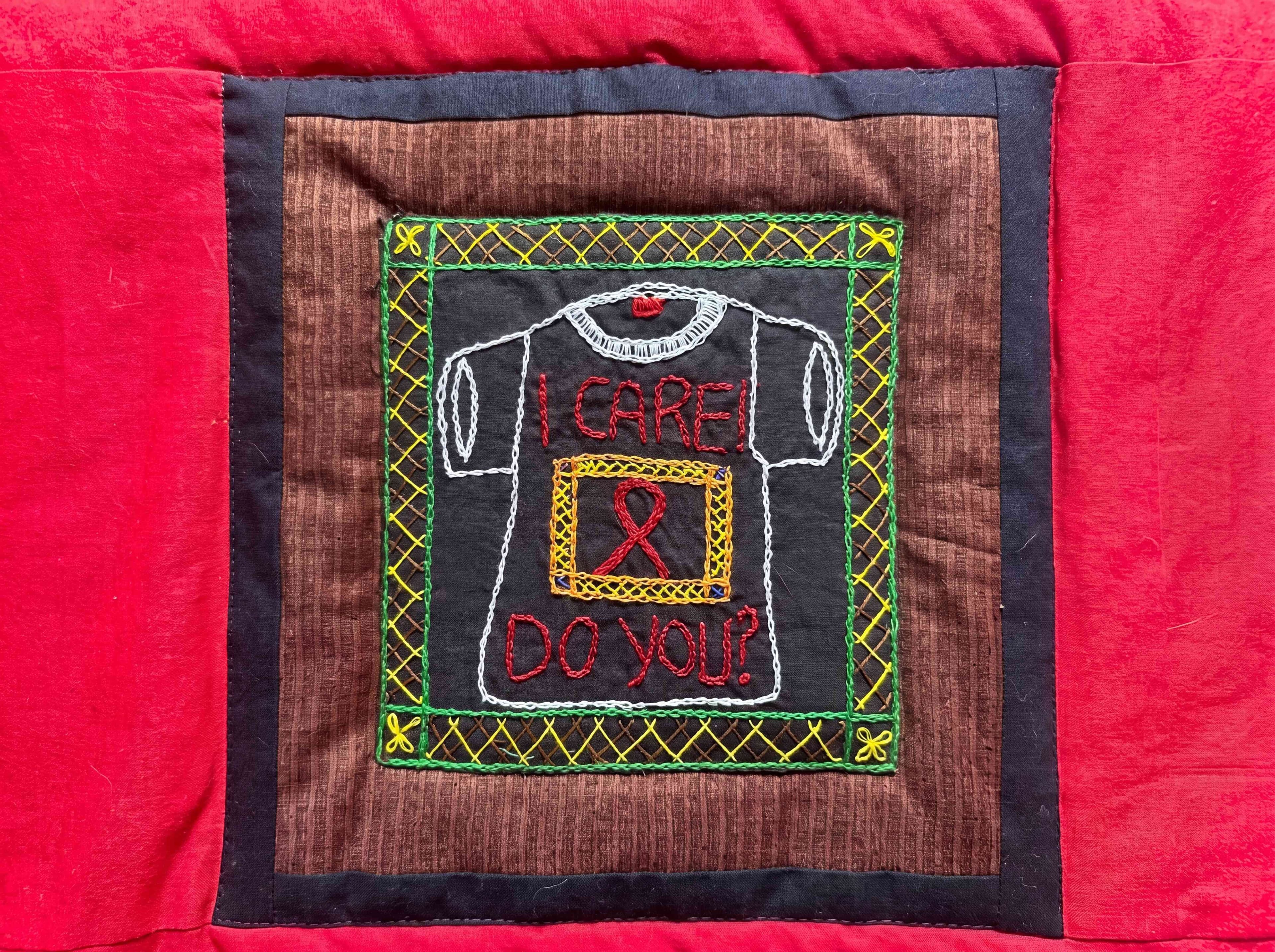 A handmade AIDS quilt panel with an embroidered T-shirt reading 'I Care! Do You?' and a red ribbon